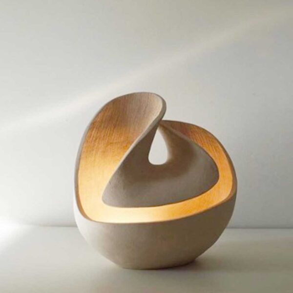 Escultural lámpara de mesa de cerámica gres con un diseño envolvente que irradia una luz cálida