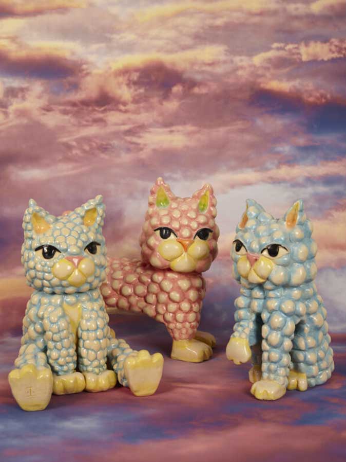 Tres figuras de gatos animados de colores vibrantes sentados bajo un cielo azul