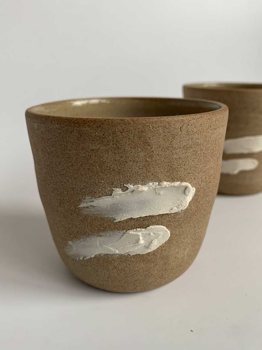 Dos tazas de arcilla de colores neutros sobre fondo blanco